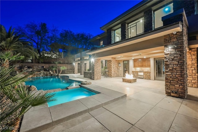 pool at night featuring a patio, a pool with connected hot tub, and an outdoor fire pit