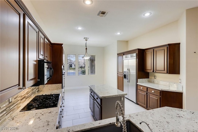 kitchen with dark brown cabinets, a center island, light stone countertops, black appliances, and decorative light fixtures