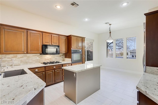 kitchen with sink, light stone counters, decorative light fixtures, a center island, and black appliances