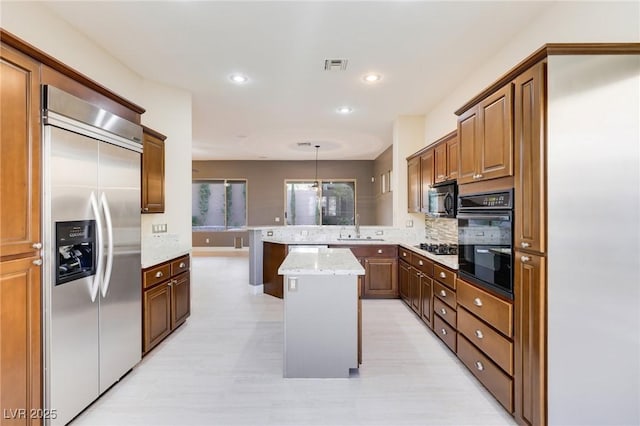 kitchen featuring pendant lighting, sink, a center island, black appliances, and light stone countertops