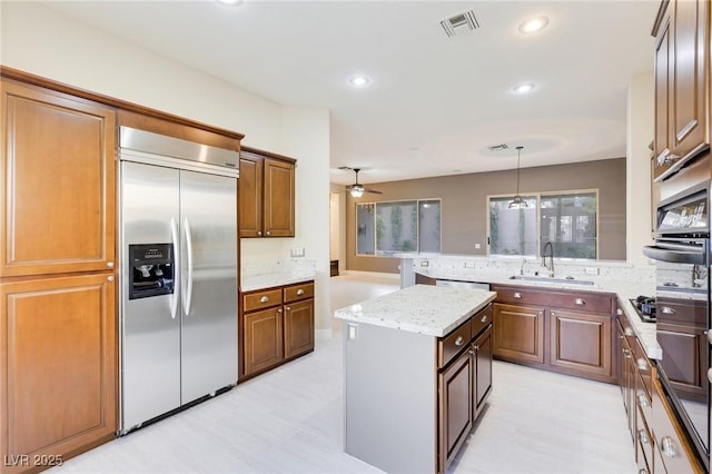 kitchen featuring built in fridge, a kitchen island, sink, hanging light fixtures, and light stone countertops