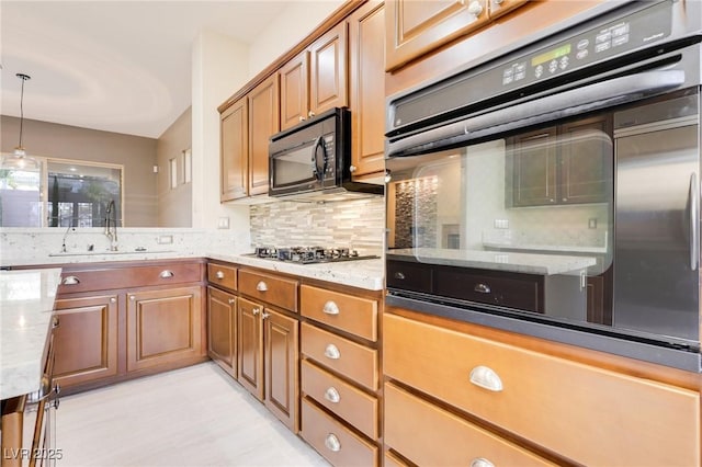 kitchen with stainless steel gas stovetop, light stone countertops, sink, and hanging light fixtures