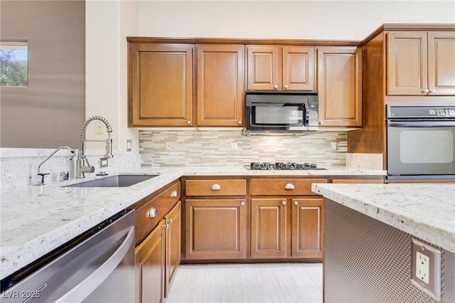 kitchen with appliances with stainless steel finishes, light stone countertops, sink, and backsplash