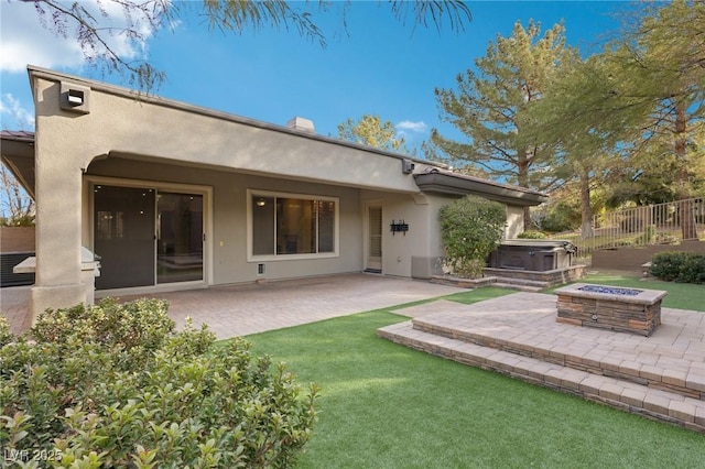 rear view of property featuring a hot tub, a patio area, and an outdoor fire pit