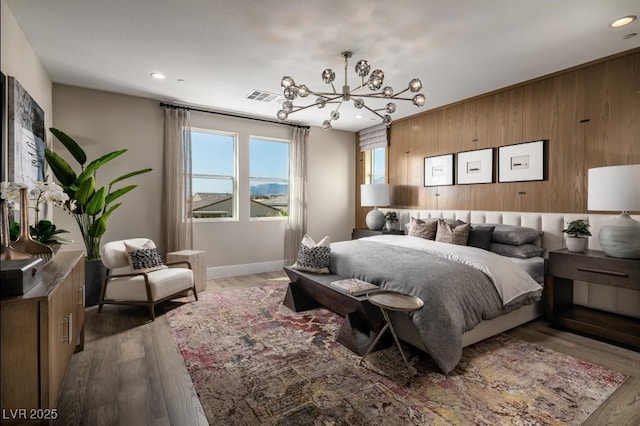 bedroom with an inviting chandelier, wooden walls, and hardwood / wood-style floors