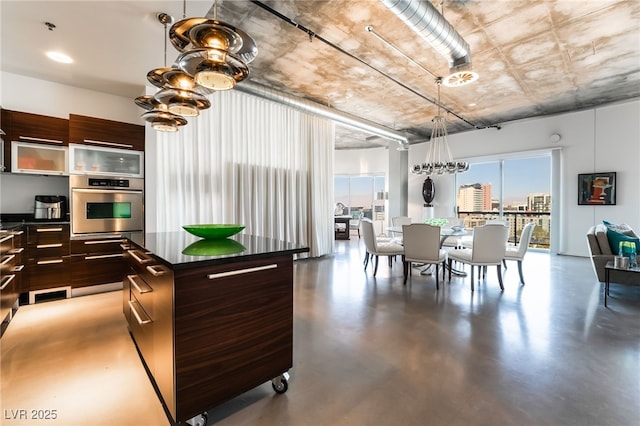 kitchen with an inviting chandelier, a center island, dark brown cabinets, concrete floors, and oven