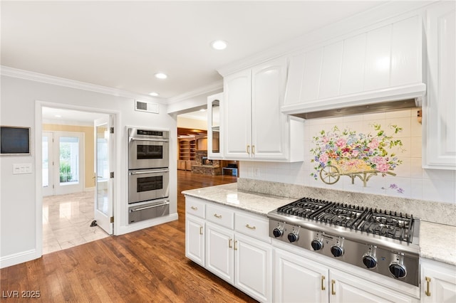 kitchen with stainless steel appliances, light stone counters, ornamental molding, white cabinets, and decorative backsplash