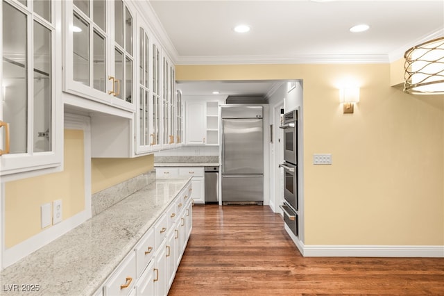 kitchen featuring dark wood-type flooring, white cabinetry, light stone counters, ornamental molding, and appliances with stainless steel finishes