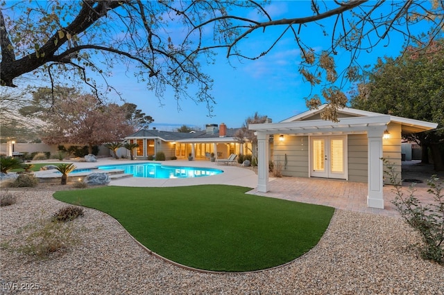 pool at dusk with french doors, a patio area, and a lawn