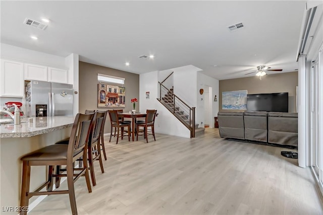 kitchen with a kitchen bar, sink, stainless steel fridge with ice dispenser, light wood-type flooring, and white cabinets