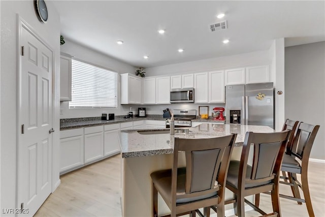 kitchen featuring a kitchen bar, white cabinetry, light wood-type flooring, appliances with stainless steel finishes, and a kitchen island with sink