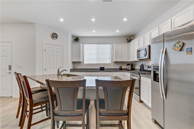 kitchen with sink, white cabinetry, a kitchen breakfast bar, stainless steel appliances, and a kitchen island with sink