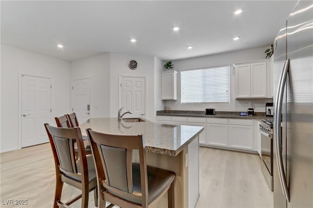 kitchen with white cabinetry, appliances with stainless steel finishes, a kitchen bar, and a center island with sink