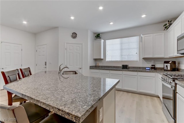 kitchen with white cabinetry, stainless steel appliances, a kitchen bar, and a center island with sink