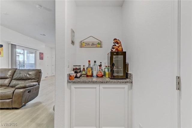 bar with white cabinetry, light stone counters, and light wood-type flooring