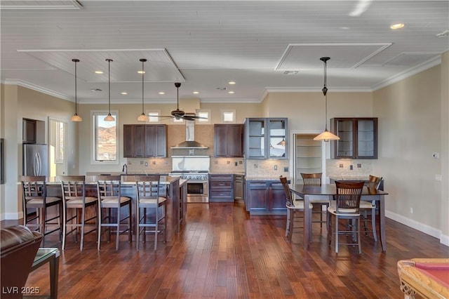 kitchen featuring wall chimney range hood, decorative light fixtures, a breakfast bar area, and appliances with stainless steel finishes