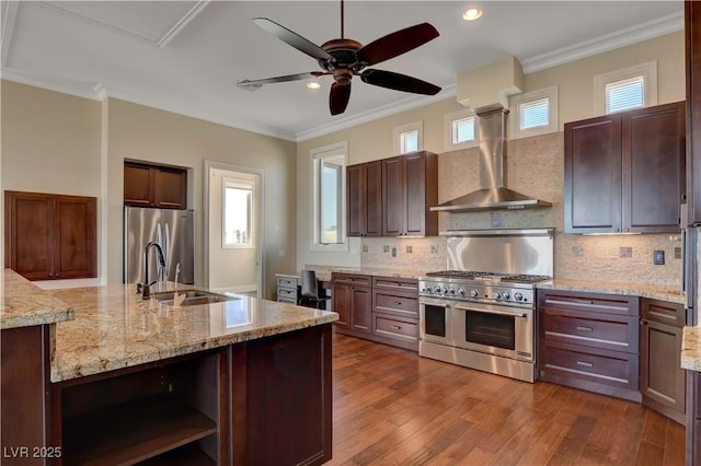 kitchen with wall chimney range hood, light stone countertops, sink, and appliances with stainless steel finishes