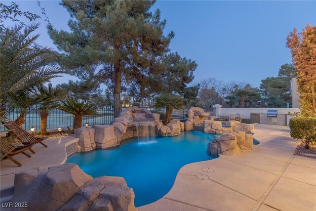 pool at dusk with exterior kitchen, grilling area, and a patio area