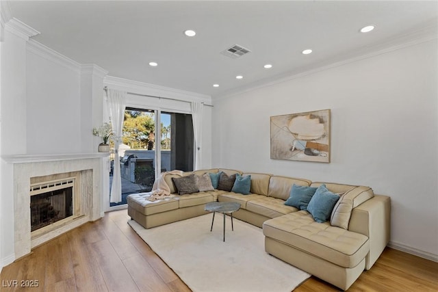 living room featuring ornamental molding, light wood-type flooring, visible vents, and a fireplace