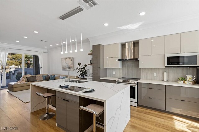 kitchen featuring gray cabinetry, a kitchen breakfast bar, a kitchen island with sink, wall chimney exhaust hood, and stainless steel electric range