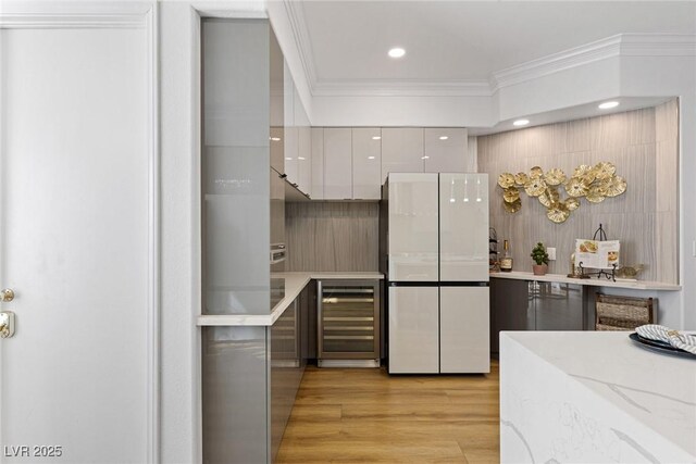 kitchen with light wood-type flooring, ornamental molding, beverage cooler, light stone countertops, and white cabinets