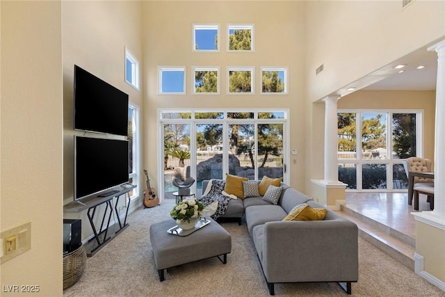 living room featuring ornate columns, a towering ceiling, and light colored carpet