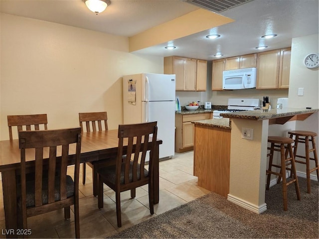 kitchen with light brown cabinetry, light stone counters, a kitchen breakfast bar, kitchen peninsula, and white appliances