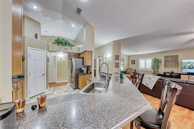 kitchen with sink, stainless steel fridge, a breakfast bar area, and light wood-type flooring