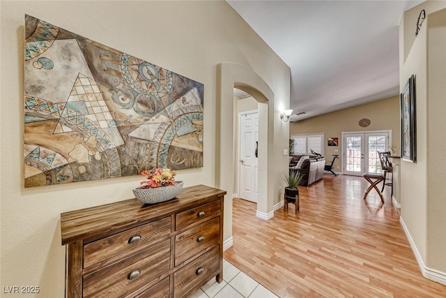 hall with lofted ceiling, light wood-type flooring, and french doors