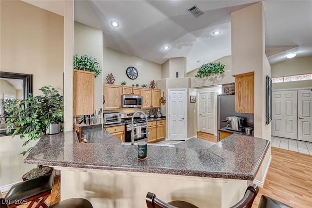 kitchen with light hardwood / wood-style flooring, appliances with stainless steel finishes, high vaulted ceiling, a kitchen bar, and kitchen peninsula