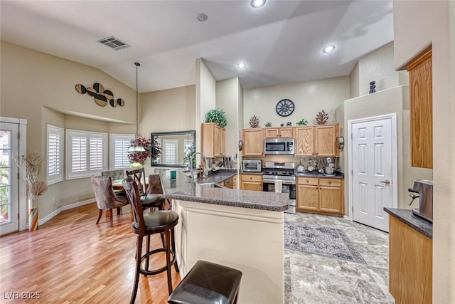 kitchen with sink, appliances with stainless steel finishes, a kitchen breakfast bar, kitchen peninsula, and pendant lighting