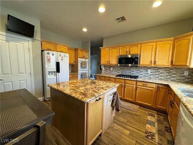 kitchen featuring white appliances, hardwood / wood-style flooring, a center island, light stone counters, and tasteful backsplash