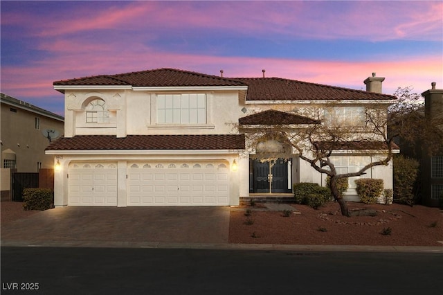 mediterranean / spanish-style home with a chimney, stucco siding, an attached garage, driveway, and a tiled roof