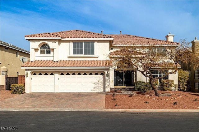 mediterranean / spanish-style house with an attached garage, a tile roof, decorative driveway, stucco siding, and a chimney