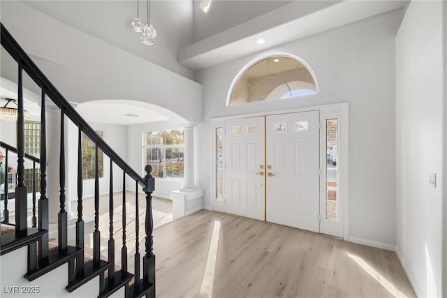 foyer entrance with a towering ceiling, light wood-style flooring, stairs, and baseboards