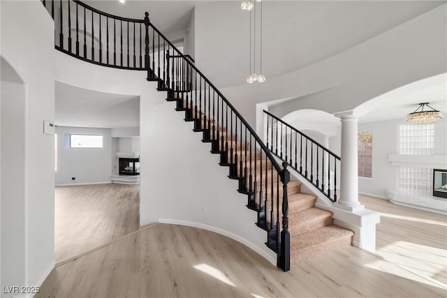 staircase featuring baseboards, wood finished floors, a multi sided fireplace, and ornate columns