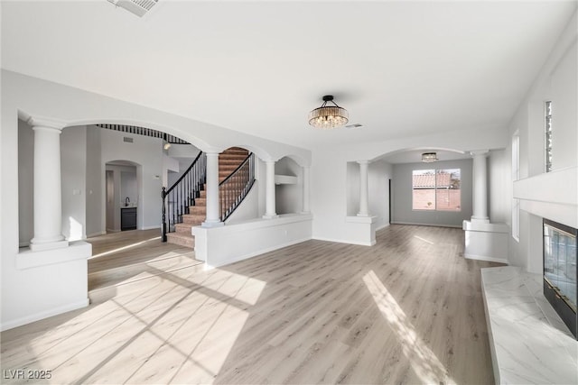 unfurnished living room with arched walkways, light wood-style flooring, stairway, and decorative columns