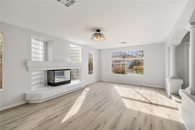 unfurnished living room featuring a tile fireplace, visible vents, plenty of natural light, and ornate columns