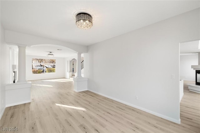 interior space featuring arched walkways, light wood-type flooring, baseboards, and ornate columns