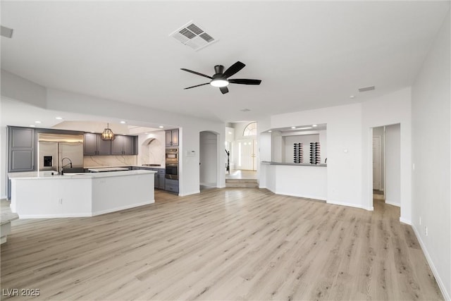 unfurnished living room featuring visible vents, arched walkways, baseboards, ceiling fan, and light wood-type flooring