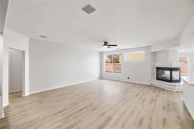 unfurnished living room with light wood finished floors, visible vents, a ceiling fan, a multi sided fireplace, and baseboards