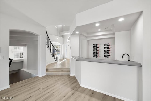 bar with light wood-style flooring, stairway, arched walkways, and recessed lighting