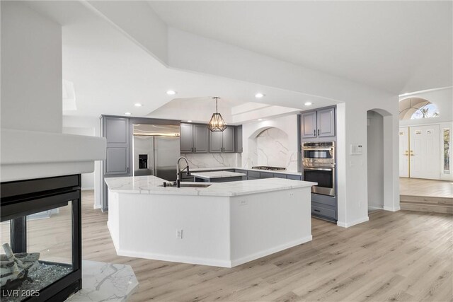 kitchen featuring a center island with sink, stainless steel appliances, a sink, and gray cabinetry