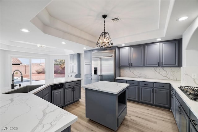 kitchen with a raised ceiling, appliances with stainless steel finishes, a center island, gray cabinetry, and a sink