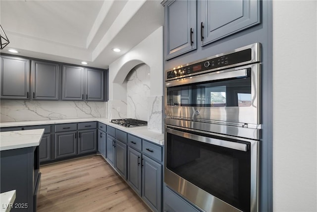 kitchen featuring appliances with stainless steel finishes, gray cabinets, light wood-style flooring, and tasteful backsplash