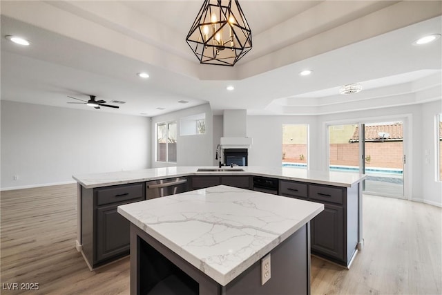 kitchen with a tray ceiling, open floor plan, a kitchen island, a sink, and dishwasher