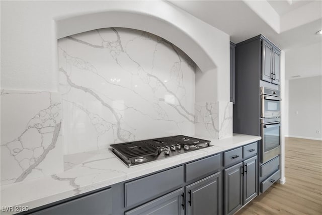 kitchen featuring stainless steel appliances, light wood-type flooring, gray cabinets, light stone countertops, and tasteful backsplash