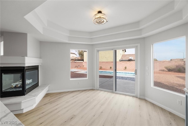 unfurnished living room featuring light wood-style floors, baseboards, a raised ceiling, and a multi sided fireplace