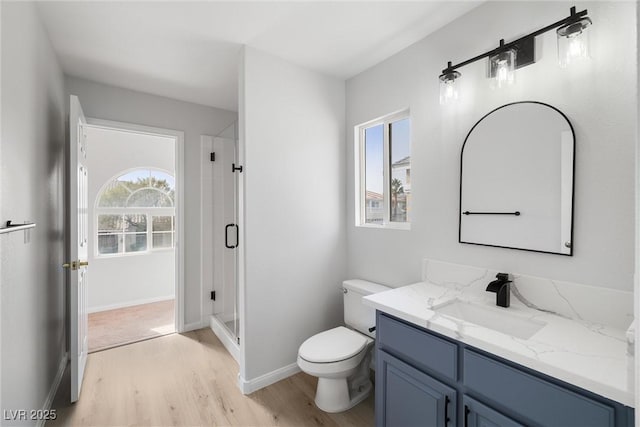 bathroom with toilet, wood finished floors, vanity, baseboards, and a stall shower