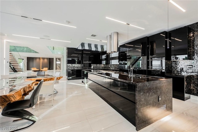 kitchen featuring double oven, an island with sink, sink, dark stone countertops, and backsplash